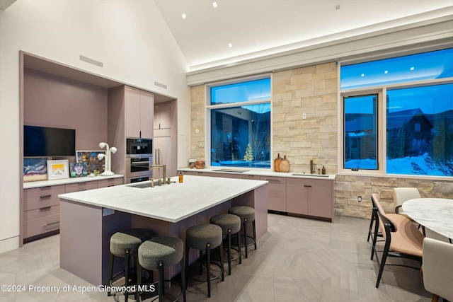 kitchen with stainless steel oven, a breakfast bar, built in microwave, lofted ceiling, and an island with sink