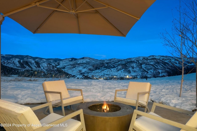 snow covered patio with a mountain view and an outdoor fire pit