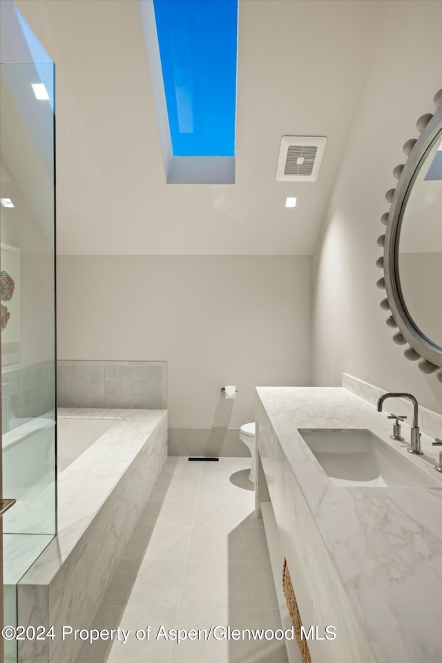 bathroom featuring a skylight, a relaxing tiled tub, tile patterned floors, toilet, and vanity