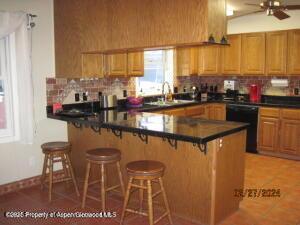 1645 E 7th St, Craig, CO 81625 - kitchen with light tile patterned floors, decorative backsplash, dishwasher, dark countertops, and a breakfast bar