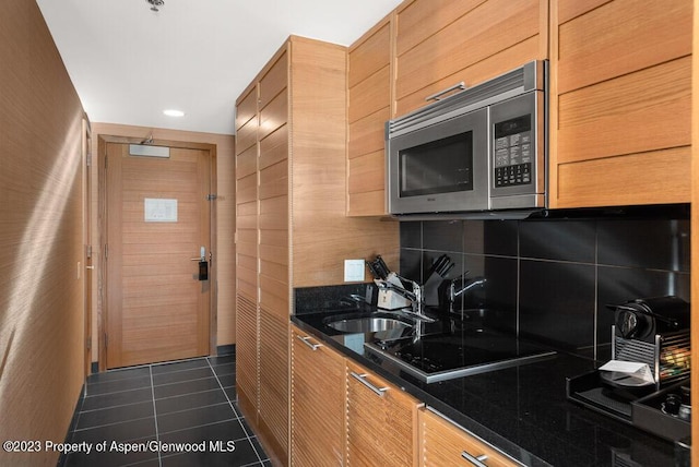 kitchen featuring tasteful backsplash, black cooktop, dark tile patterned floors, and sink