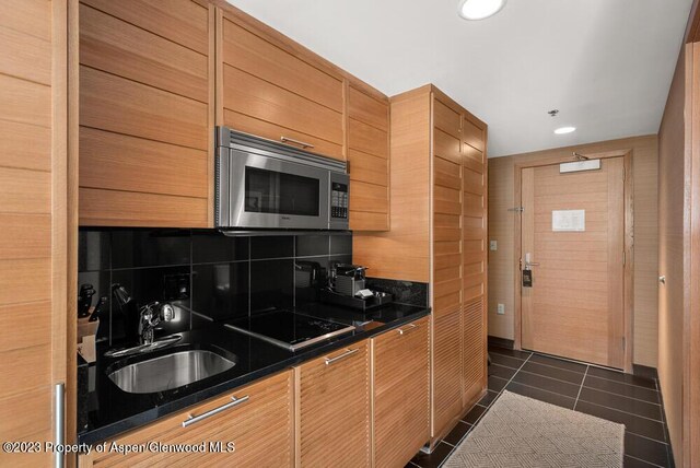 kitchen with dark tile patterned floors, black electric cooktop, sink, and tasteful backsplash