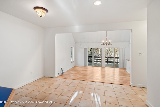 tiled spare room with vaulted ceiling and a notable chandelier