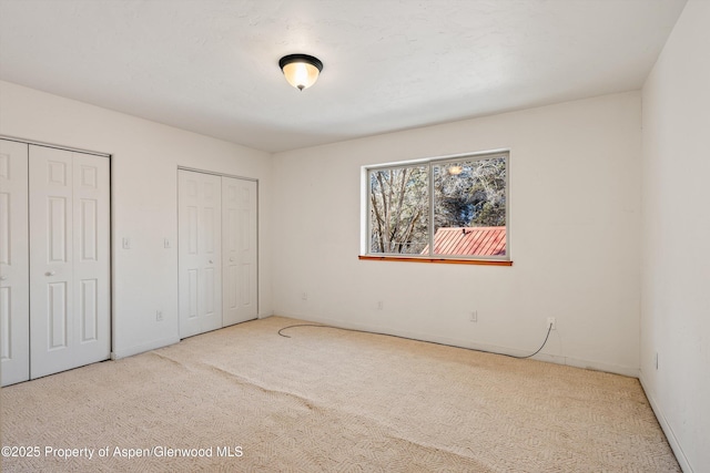 unfurnished bedroom featuring carpet flooring and multiple closets