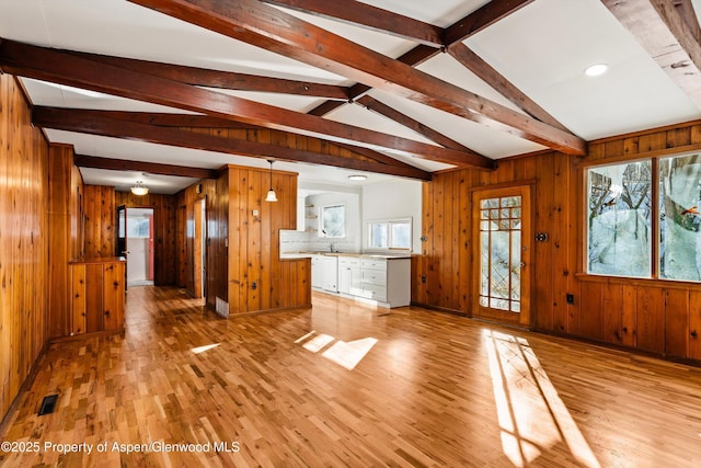 unfurnished living room featuring vaulted ceiling with beams, wood walls, and light hardwood / wood-style flooring