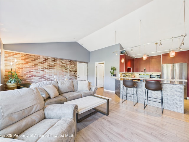 living room featuring brick wall, vaulted ceiling, light wood-style flooring, and baseboards