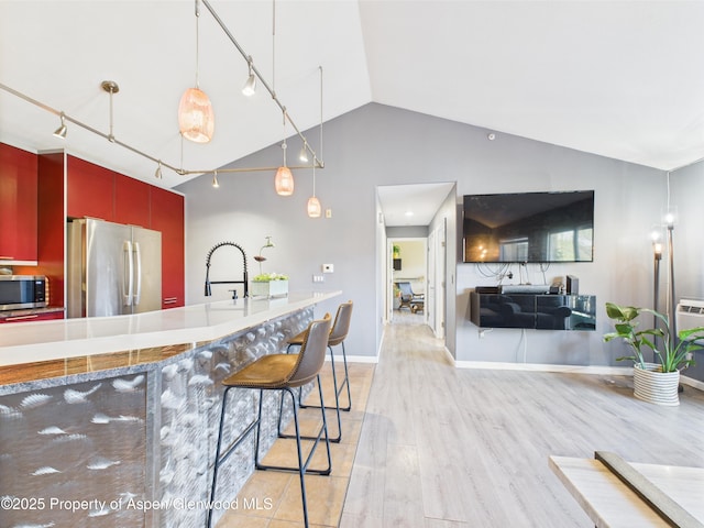 kitchen featuring a sink, appliances with stainless steel finishes, vaulted ceiling, red cabinets, and light wood-style floors