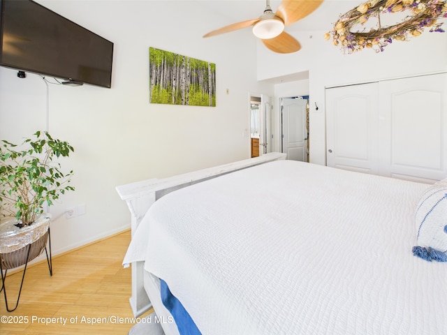 bedroom with a closet, baseboards, ceiling fan, light wood-style floors, and a high ceiling