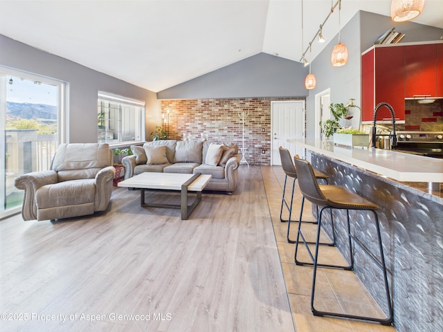 living area featuring light wood finished floors, brick wall, and vaulted ceiling
