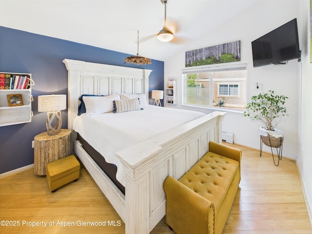 bedroom featuring light wood finished floors, lofted ceiling, a baseboard radiator, and baseboards