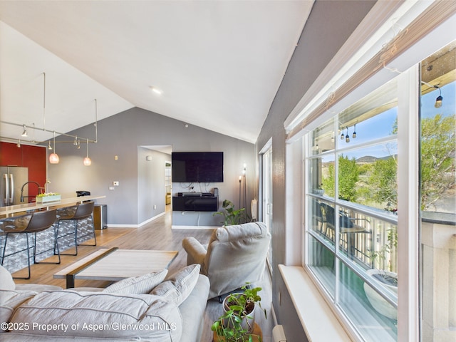 living room featuring baseboards, light wood-style floors, track lighting, and vaulted ceiling