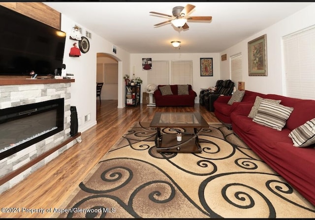 living room featuring a stone fireplace, ceiling fan, and hardwood / wood-style floors