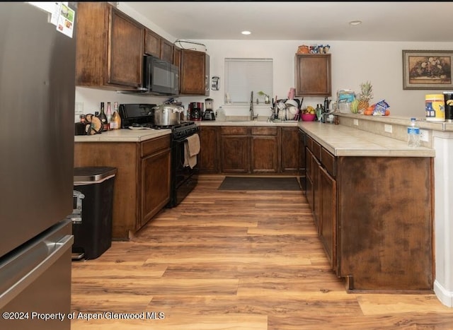 kitchen featuring kitchen peninsula, dark brown cabinetry, sink, black appliances, and light hardwood / wood-style floors