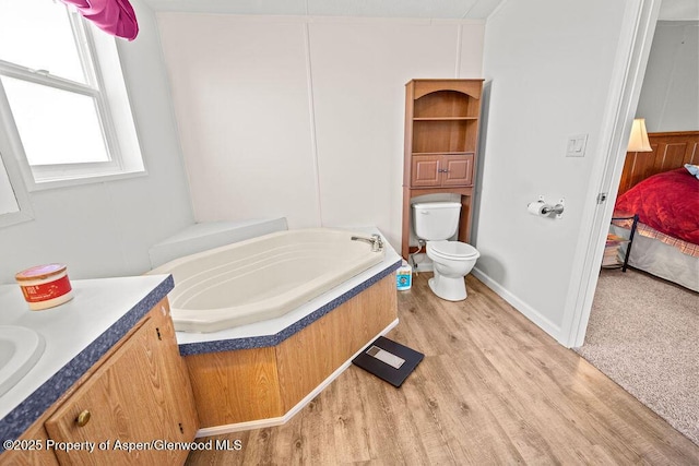 ensuite bathroom featuring a garden tub, wood finished floors, toilet, and vanity
