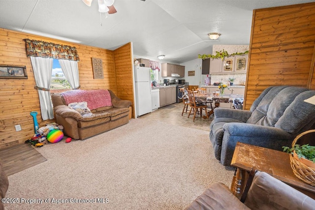 living area with ceiling fan, vaulted ceiling, and wooden walls