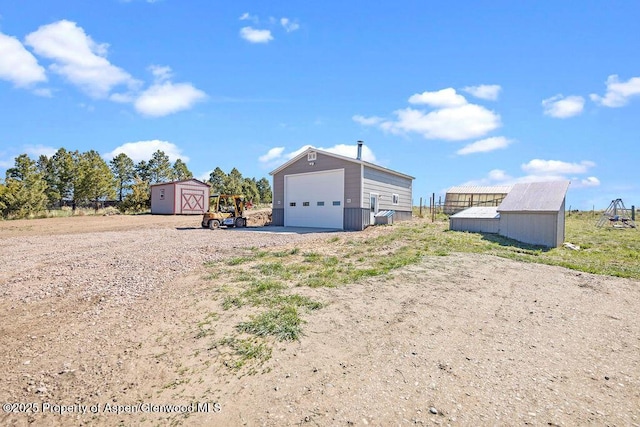 view of yard featuring a detached garage, an outbuilding, a shed, and dirt driveway