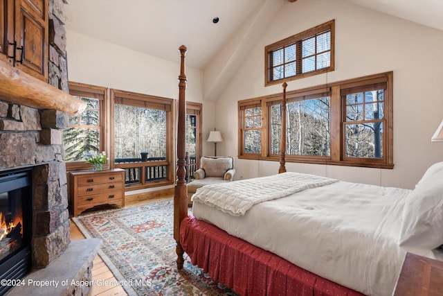 bedroom with beamed ceiling, high vaulted ceiling, hardwood / wood-style flooring, and a stone fireplace