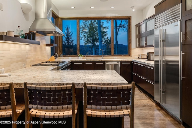 kitchen featuring a kitchen bar, island exhaust hood, kitchen peninsula, stainless steel appliances, and light stone countertops