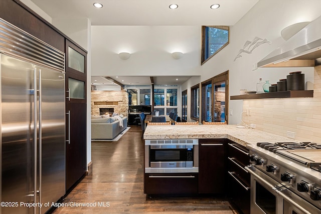 kitchen featuring built in appliances, dark brown cabinets, dark hardwood / wood-style floors, and tasteful backsplash