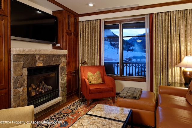 living area with crown molding, hardwood / wood-style flooring, and a stone fireplace