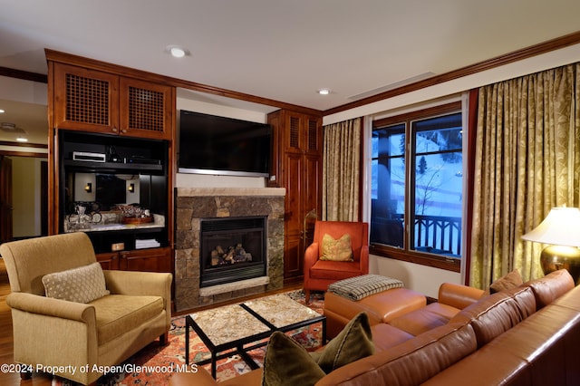 living room featuring hardwood / wood-style floors, ornamental molding, and a stone fireplace