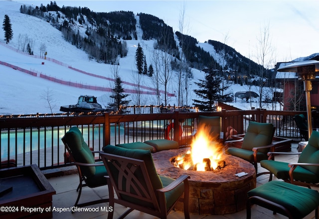 snow covered deck featuring a mountain view, an outdoor fire pit, and a swimming pool