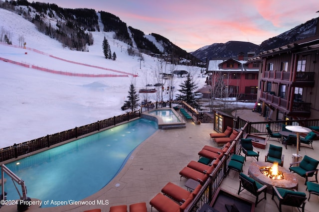 snow covered pool with a mountain view, a patio area, an outdoor fire pit, and an in ground hot tub