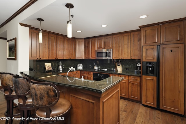 kitchen featuring black appliances, a kitchen bar, kitchen peninsula, hardwood / wood-style flooring, and hanging light fixtures