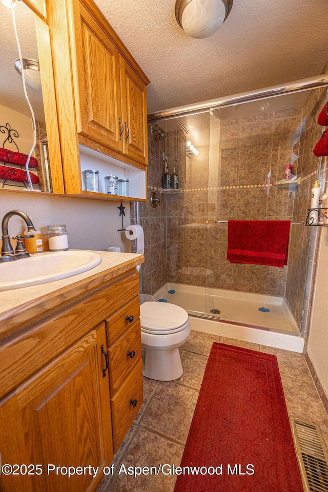 bathroom featuring vanity, an enclosed shower, a textured ceiling, and toilet