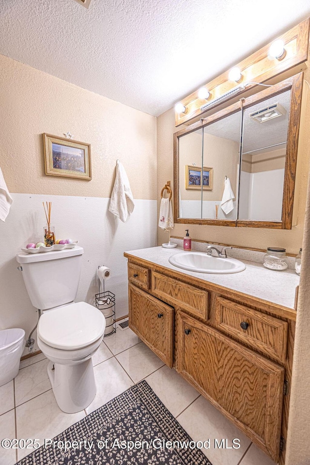 bathroom featuring tile patterned flooring, vanity, toilet, and a textured ceiling