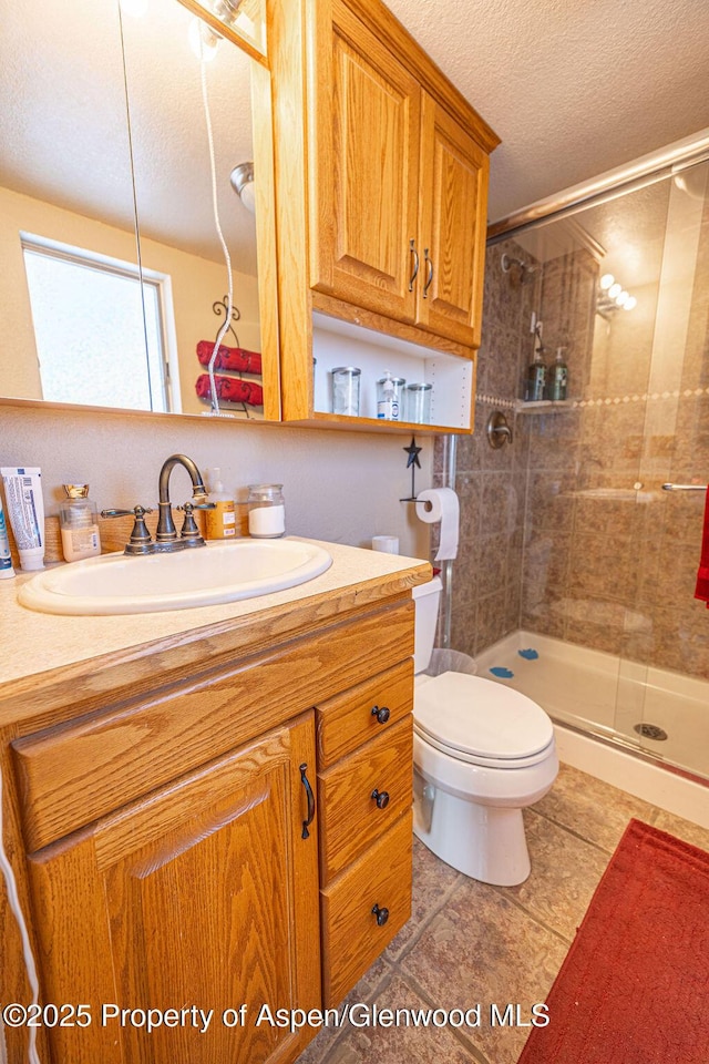 bathroom featuring vanity, a shower with door, tile patterned floors, toilet, and a textured ceiling