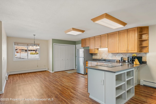 kitchen with kitchen peninsula, stainless steel fridge, tasteful backsplash, a baseboard heating unit, and pendant lighting