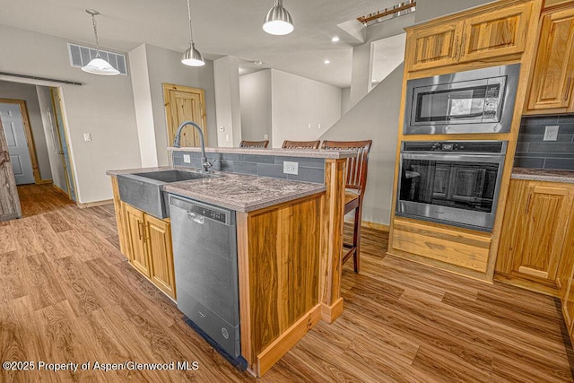 118 Highland Dr, Craig, CO 81625 - kitchen with appliances with stainless steel finishes, light wood-type flooring, an island with sink, a kitchen bar, and pendant lighting
