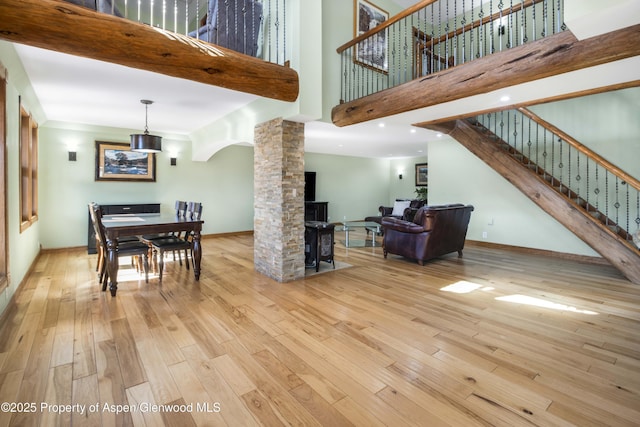 living room with decorative columns, baseboards, a towering ceiling, stairs, and light wood-style floors