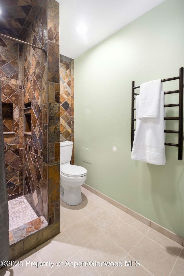 bathroom featuring toilet, a stall shower, tile patterned flooring, and baseboards