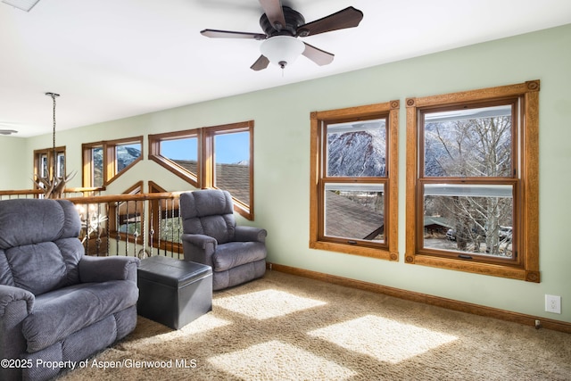 living area with ceiling fan with notable chandelier, carpet flooring, and baseboards