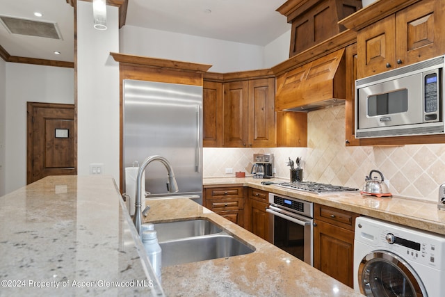 kitchen featuring sink, tasteful backsplash, light stone counters, built in appliances, and washer / dryer