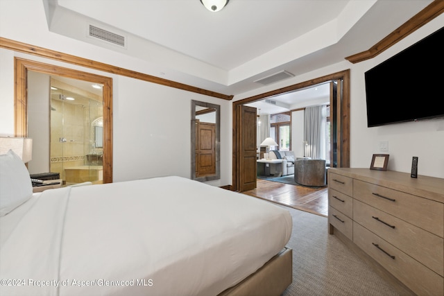 bedroom featuring a raised ceiling, wood-type flooring, and connected bathroom