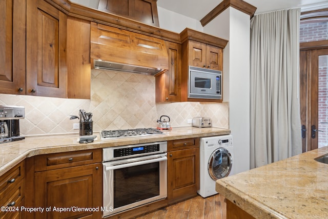 kitchen featuring tasteful backsplash, stainless steel appliances, washer / clothes dryer, and light hardwood / wood-style floors