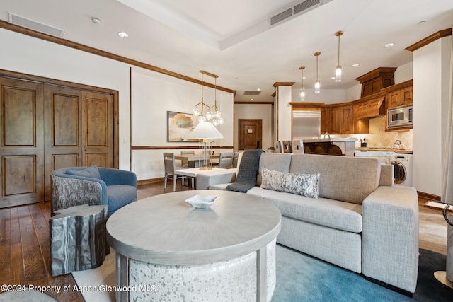 living room featuring washer / dryer, dark hardwood / wood-style floors, an inviting chandelier, and ornamental molding