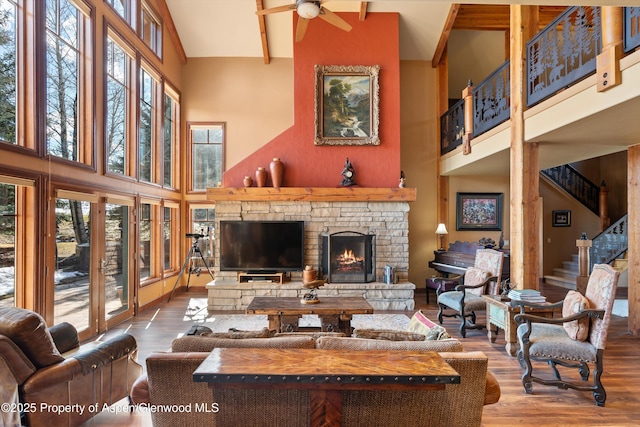 living room with a stone fireplace, wood finished floors, a towering ceiling, a ceiling fan, and stairs