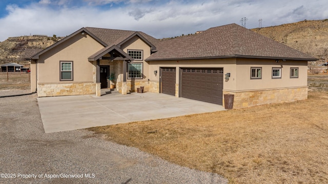 view of front of home with a garage, stone siding, driveway, and stucco siding