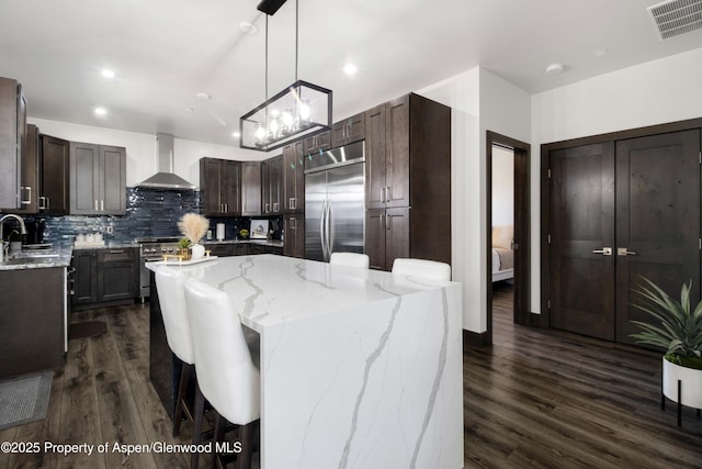 kitchen with a center island, visible vents, appliances with stainless steel finishes, wall chimney range hood, and dark brown cabinets