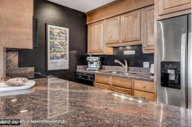 kitchen featuring a textured wall, light brown cabinets, a sink, dark stone countertops, and stainless steel fridge