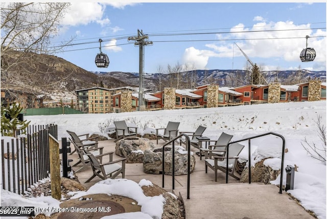 snow covered patio featuring an outdoor fire pit, fence, and a mountain view