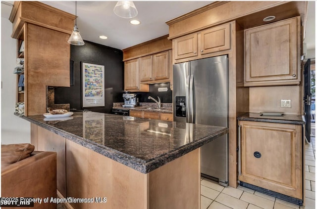 kitchen featuring light tile patterned floors, a peninsula, a sink, light brown cabinetry, and stainless steel fridge