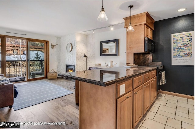 kitchen featuring a large fireplace, black microwave, open floor plan, and brown cabinetry