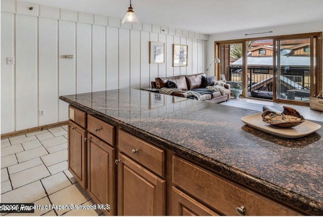 kitchen with hanging light fixtures, dark stone counters, brown cabinetry, and open floor plan