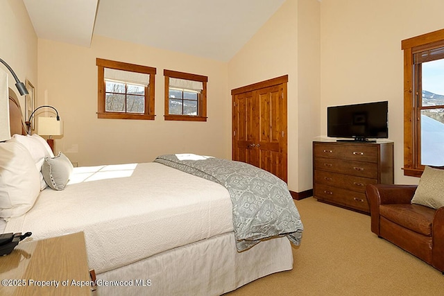 bedroom featuring multiple windows, light colored carpet, lofted ceiling, and a closet