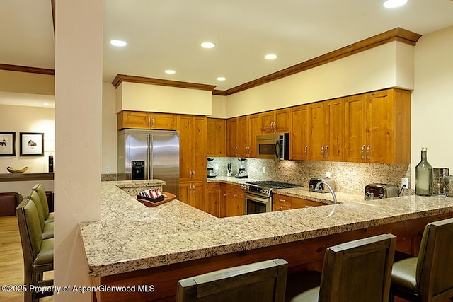 kitchen with appliances with stainless steel finishes, light stone counters, a kitchen breakfast bar, and kitchen peninsula